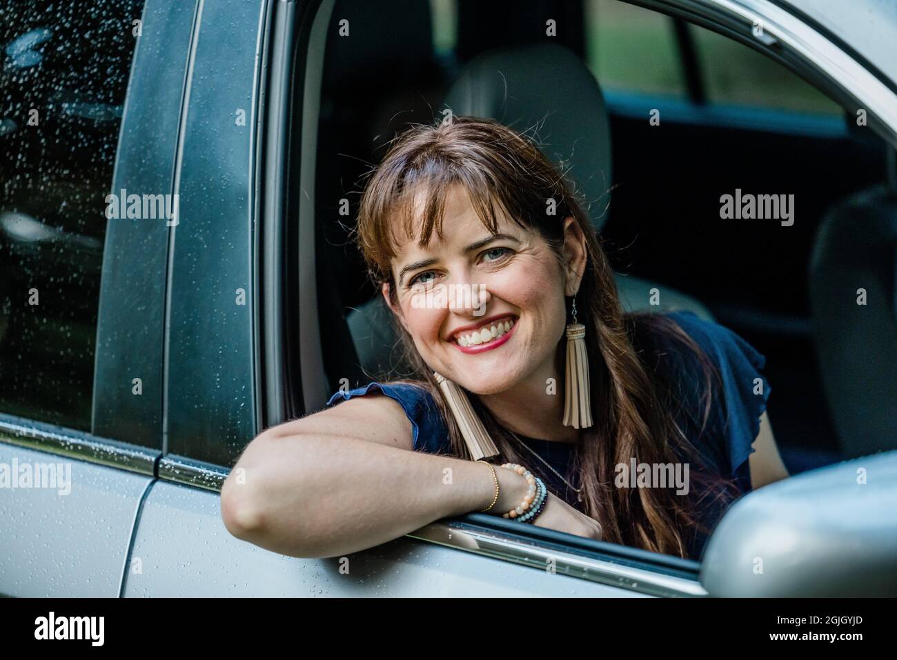 Una donna con un abito in camicia blu marina che guarda fuori da un finestrino dell'auto Foto Stock