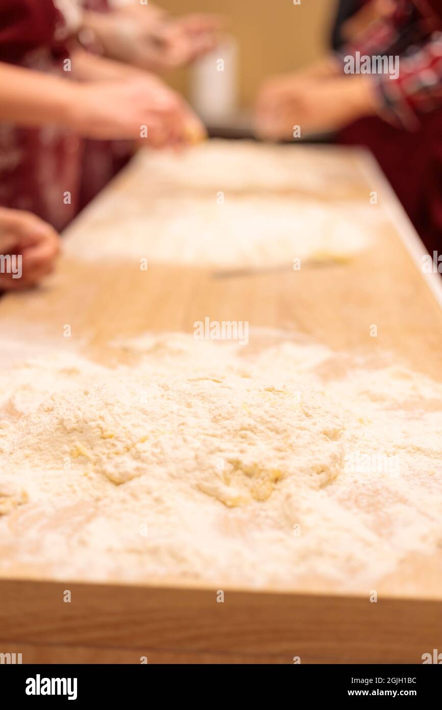 Le mani di molte persone impastano l'impasto sul tavolo. Mescolare un uovo crudo con la farina. Primo piano. Foto Stock