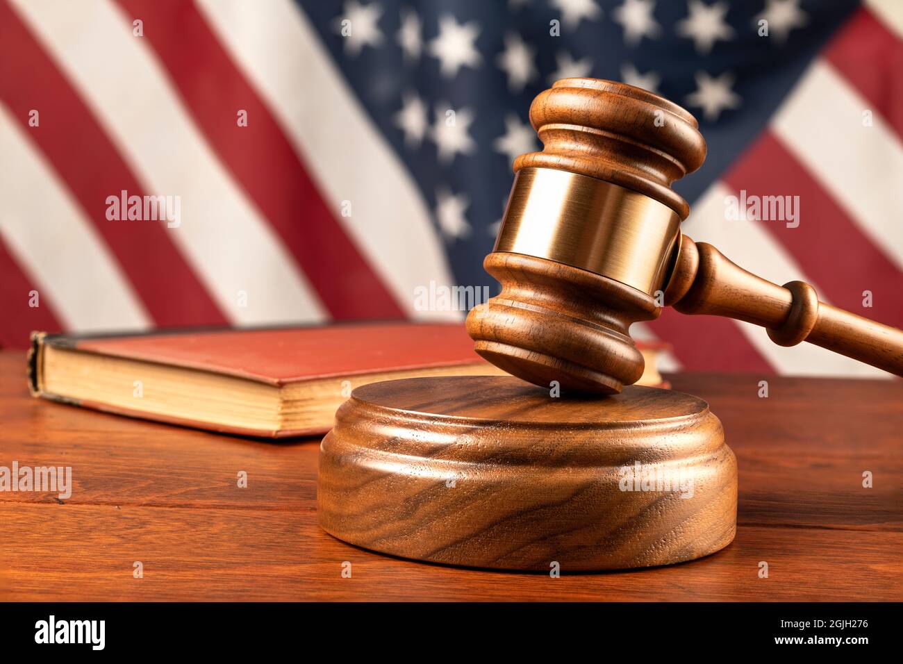 Un gavel e blocco di legno riposano in cima alla scrivania di un giudice con un libro legale e bandiera americana sfondo. Foto Stock
