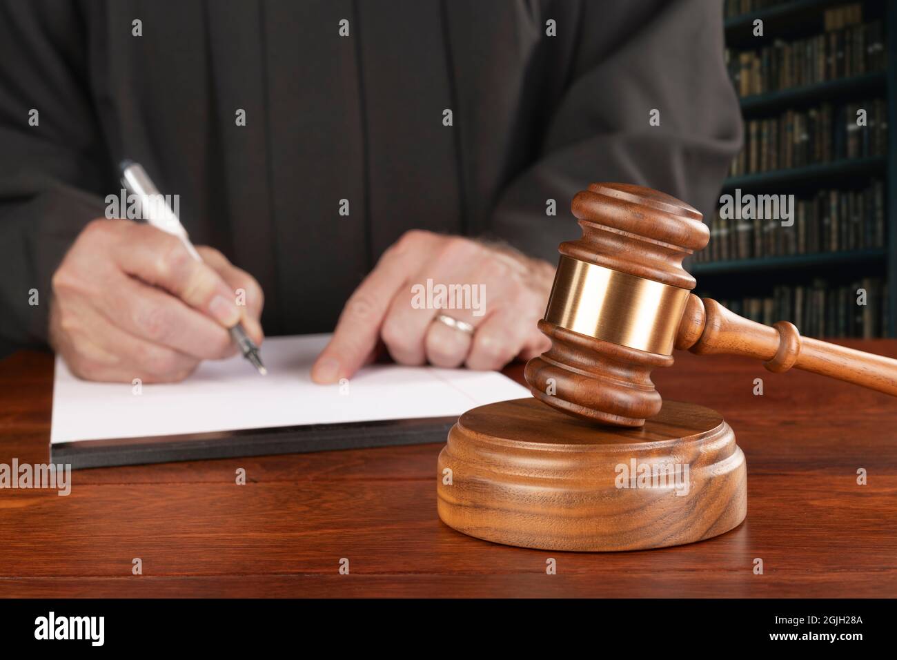 Un gavel e un blocco si trovano sulla scrivania di un giudice mentre il magistrato prende appunti nella sua biblioteca di legge preparandosi a sorvegliare un caso. Ideale per le inferenze legali. Foto Stock