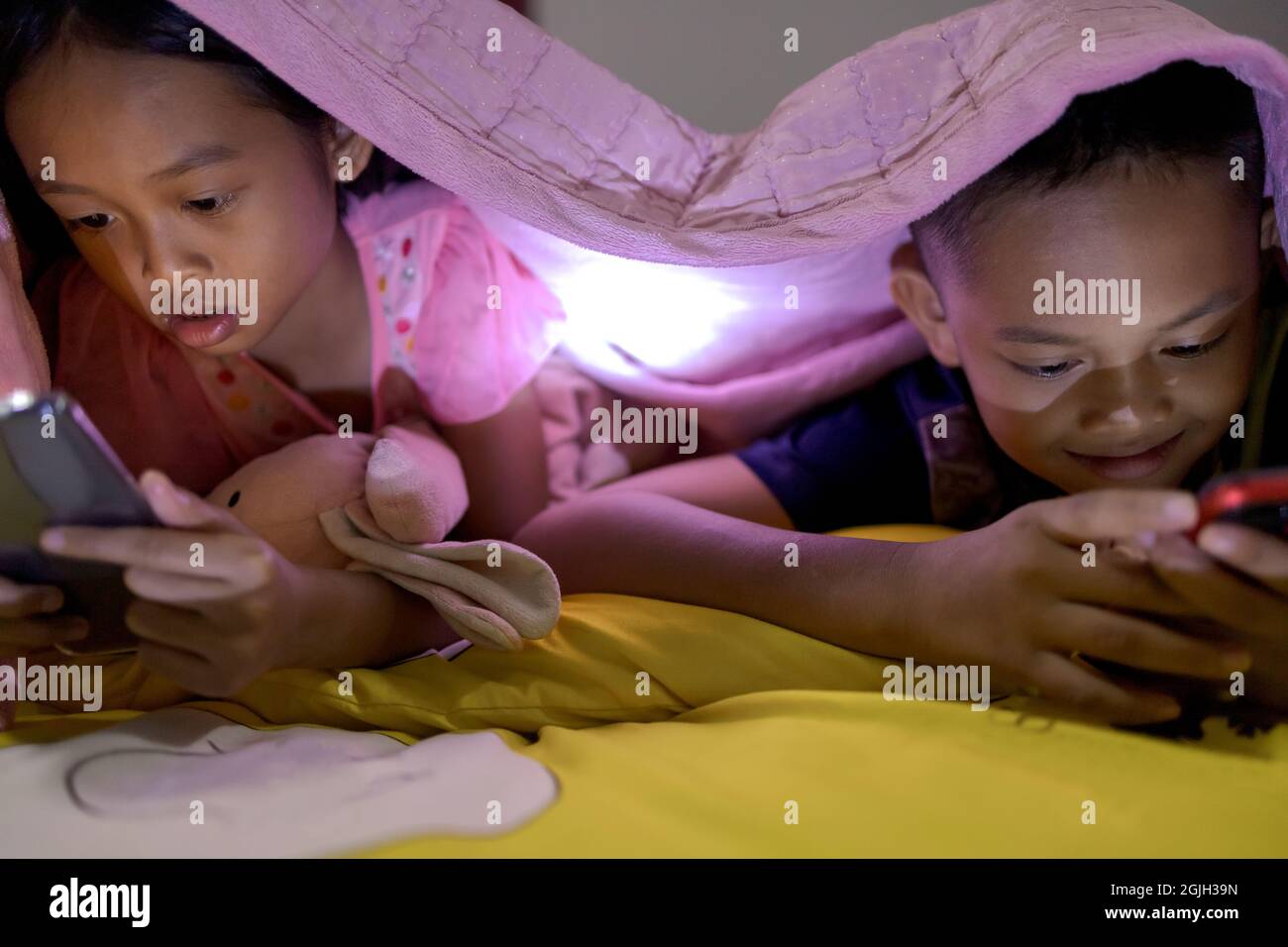 Fratello e sorella stanno usando felicemente gli smartphone a letto di notte. Foto Stock