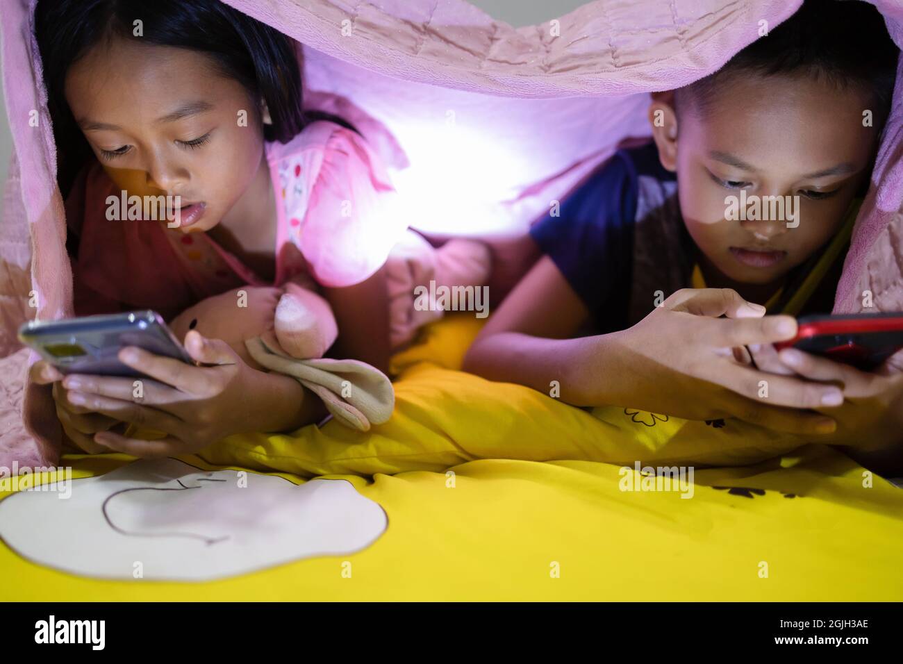 Fratello e sorella stanno usando felicemente gli smartphone a letto di notte. Foto Stock