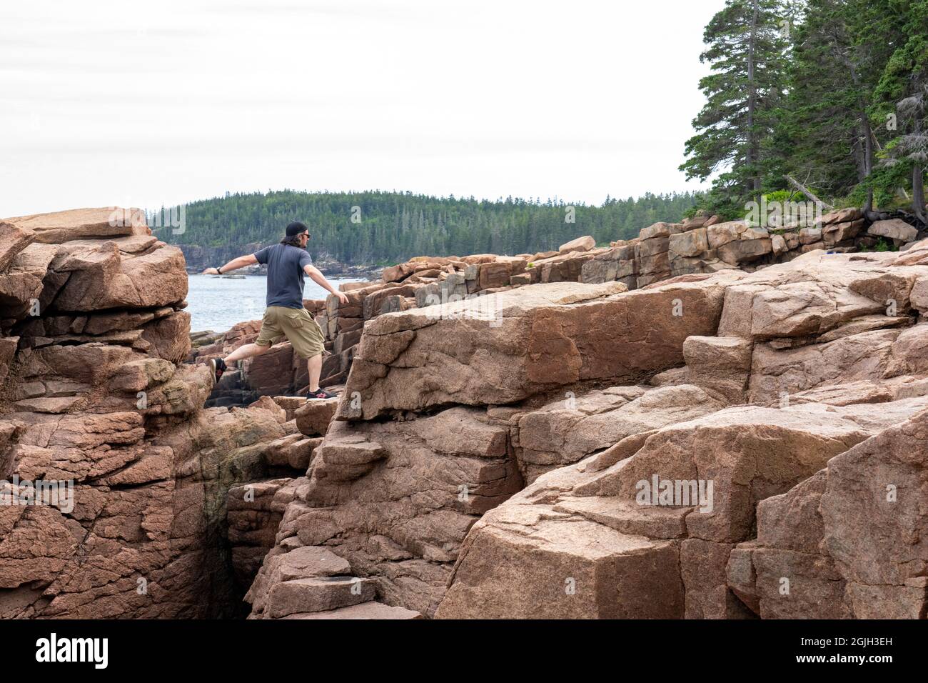 Acadia National Park, Maine, USA. Uomo che salta da una scogliera all'altra vicino a Thunder Hole. Foto Stock
