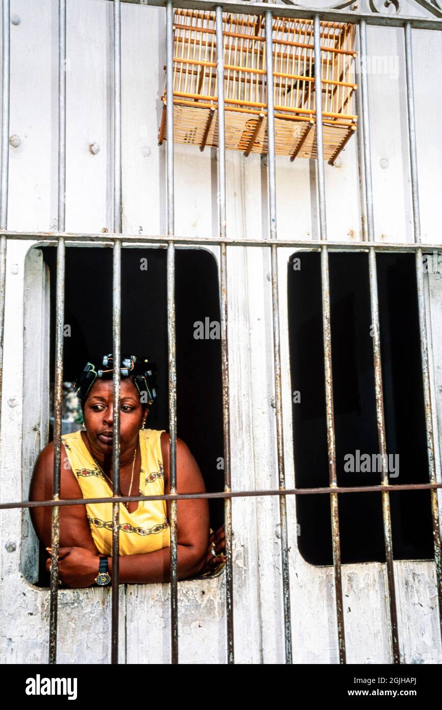 Donna cubana con uccello in gabbia d'uccello, guardando attraverso le finestre della sua casa, Sancti Spiritus, Cuba Foto Stock