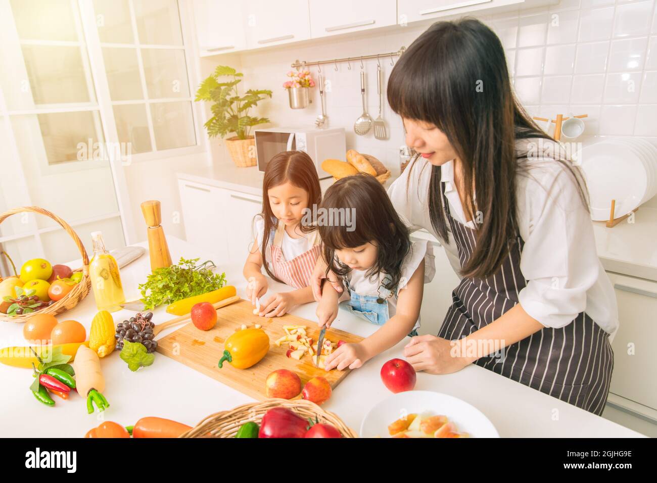 Bambina goda giocare la mela tagliata insieme con la madre e la sorella nella cucina domestica. Foto Stock