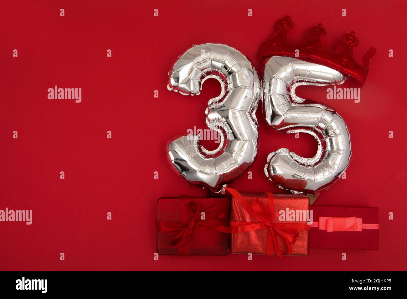 Palloncini d'aria in lamina d'argento che mostrano il numero di trentacinque 35 posti su sfondo rosso con i regali avvolti per il concetto di anniversario di compleanno Foto Stock