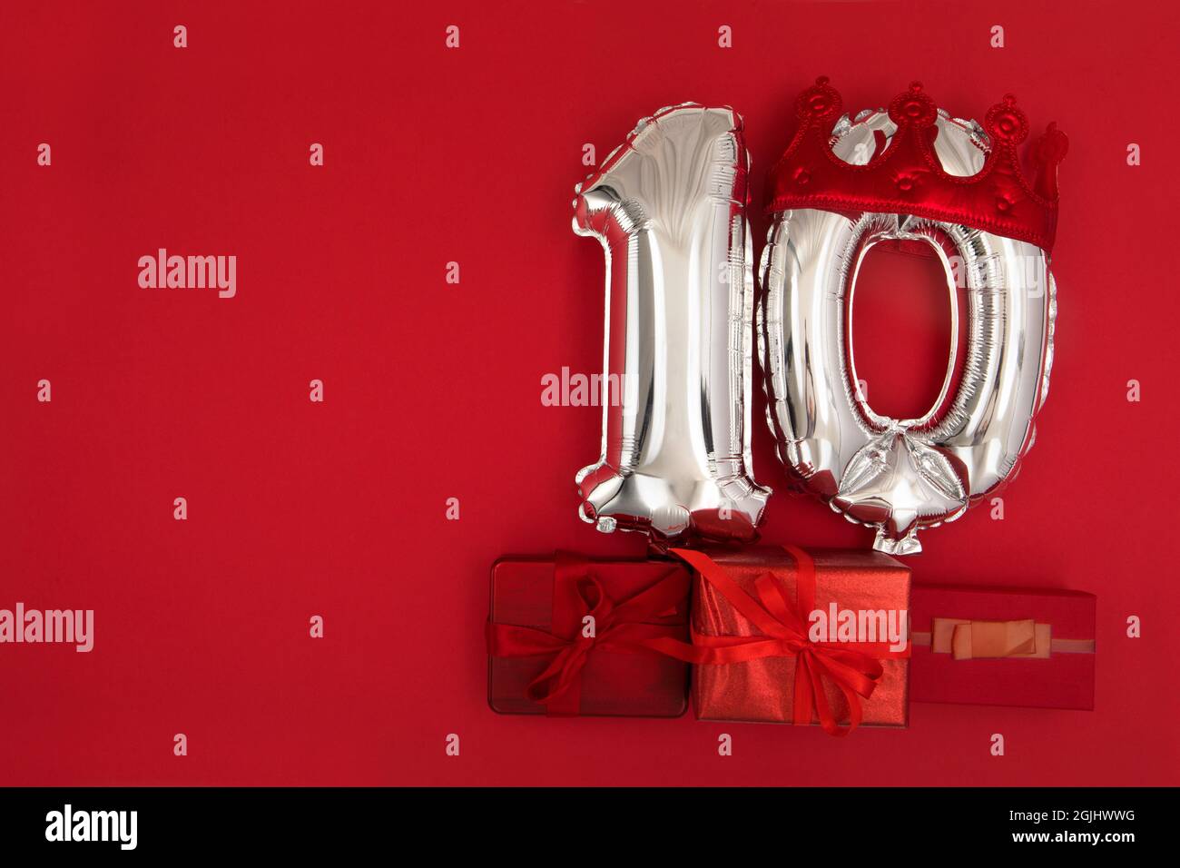 Palloncini d'aria in lamina d'argento che mostrano il numero 10 dieci posti su sfondo rosso con i regali avvolti per il concetto di anniversario di compleanno Foto Stock