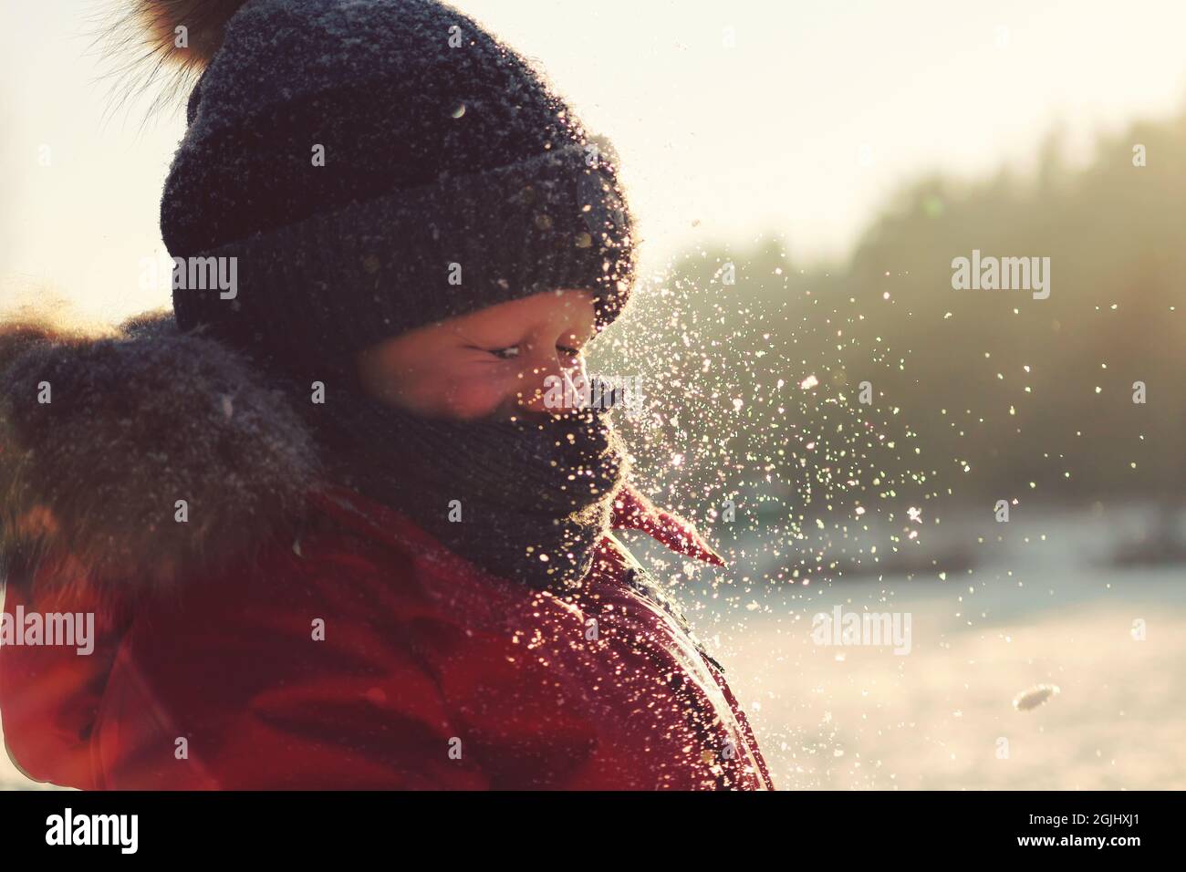 I fiocchi di neve brillano alla luce del sole nell'aria davanti al volto di un bambino che ha chiuso gli occhi. Un ragazzo in inverno gioca con la neve all'aperto Foto Stock