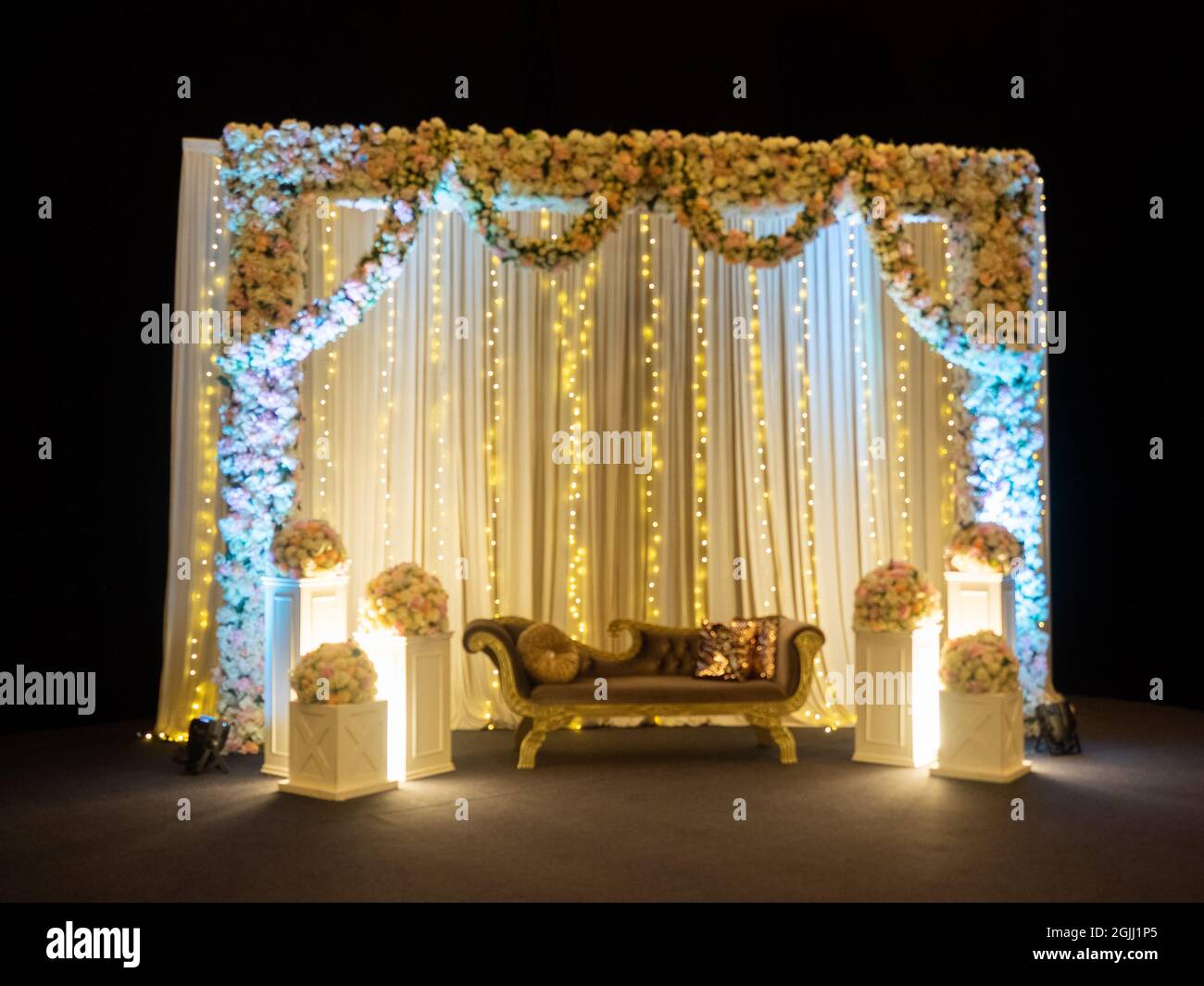 Zona foto matrimonio decorazione alleggerita con tende bianche, pali con fiori e un divano Foto Stock