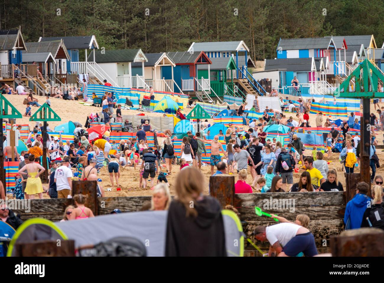 Wells-next-the-Sea North Norfolk, Regno Unito, famiglie sulla spiaggia affollata con capanne colorate sullo sfondo Foto Stock