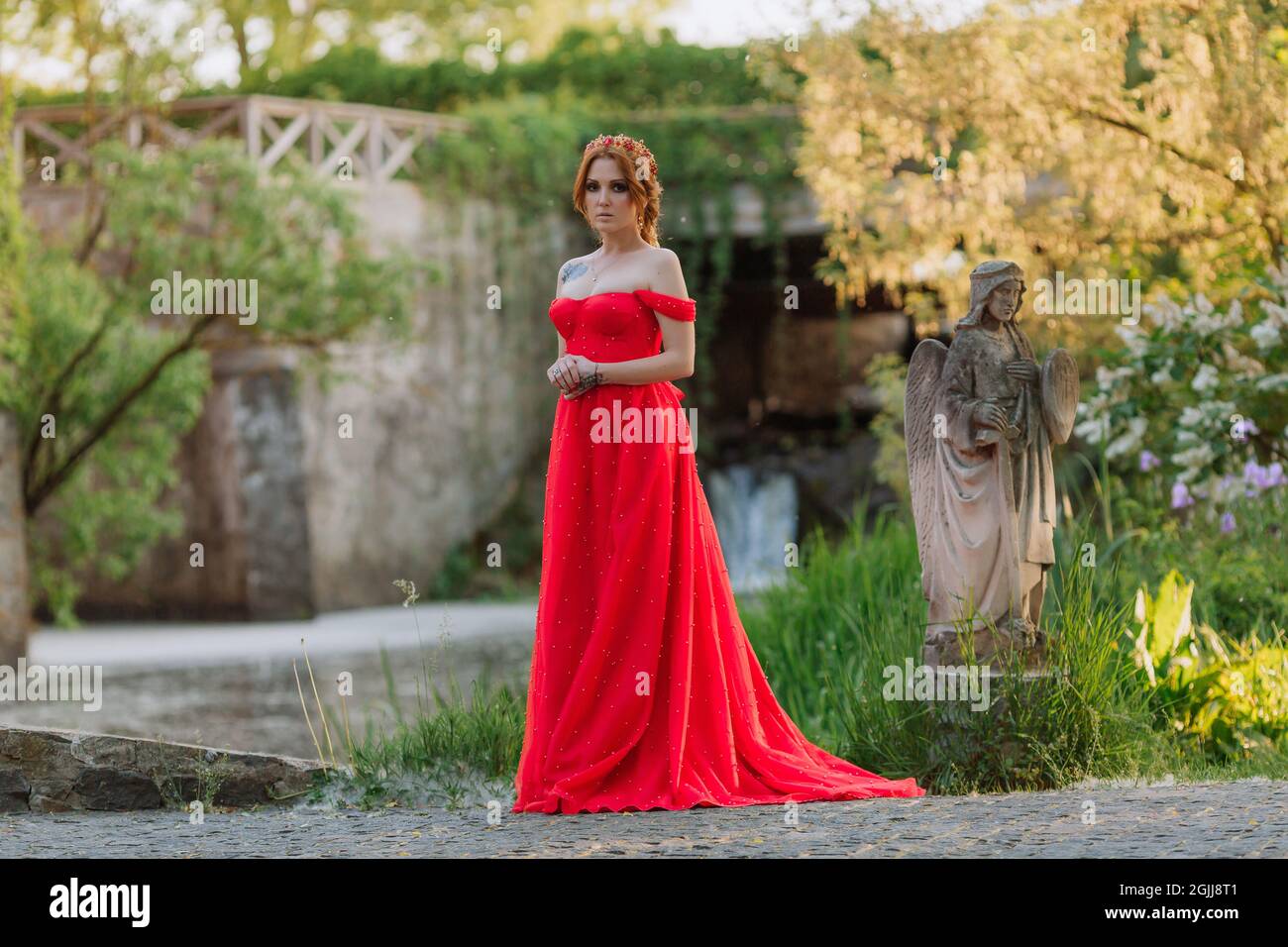 Bella donna tattoed rosso in lungo vestito rosso che posa vicino al castello Foto Stock