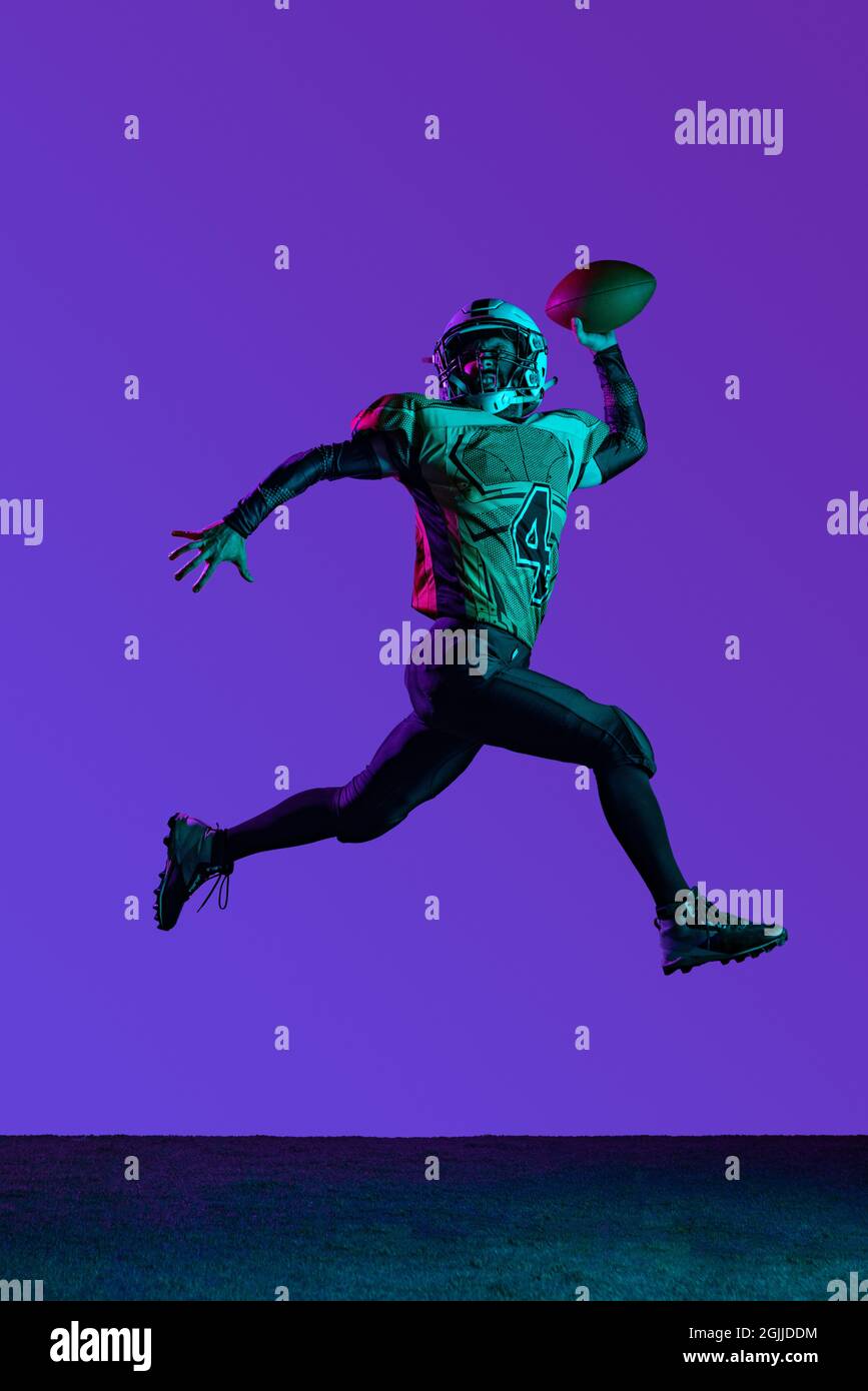 Ritratto a tutta lunghezza di maschio american fotball giocatore formazione isolato su sfondo viola scuro studio Foto Stock