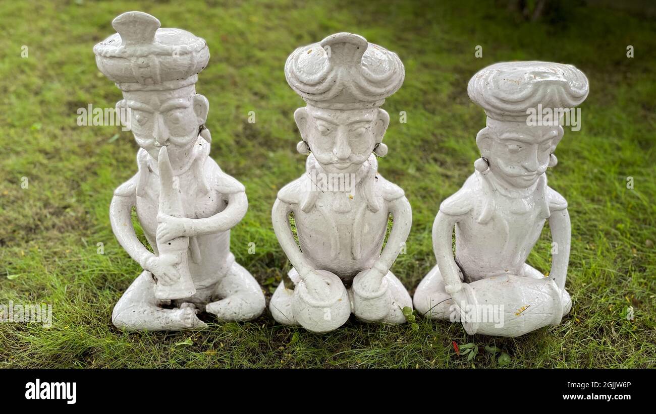 Tre idoli di colore bianco di forma umana che si sifano sull'erba e suonano strumenti musicali classici Foto Stock