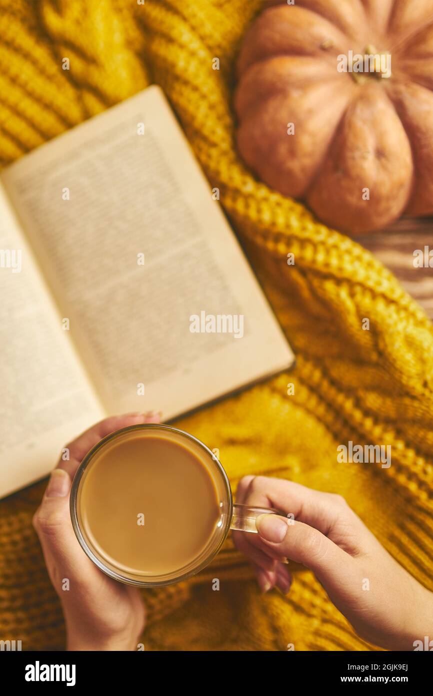 Caffè fragrante nelle mani delle donne, un libro di storie sul maglione a maglia. Vista dall'alto di uno sfondo romantico. Zucca rotonda matura. Composizione autunnale per biglietti d'auguri e inviti. Autunno ancora vita. Foto Stock