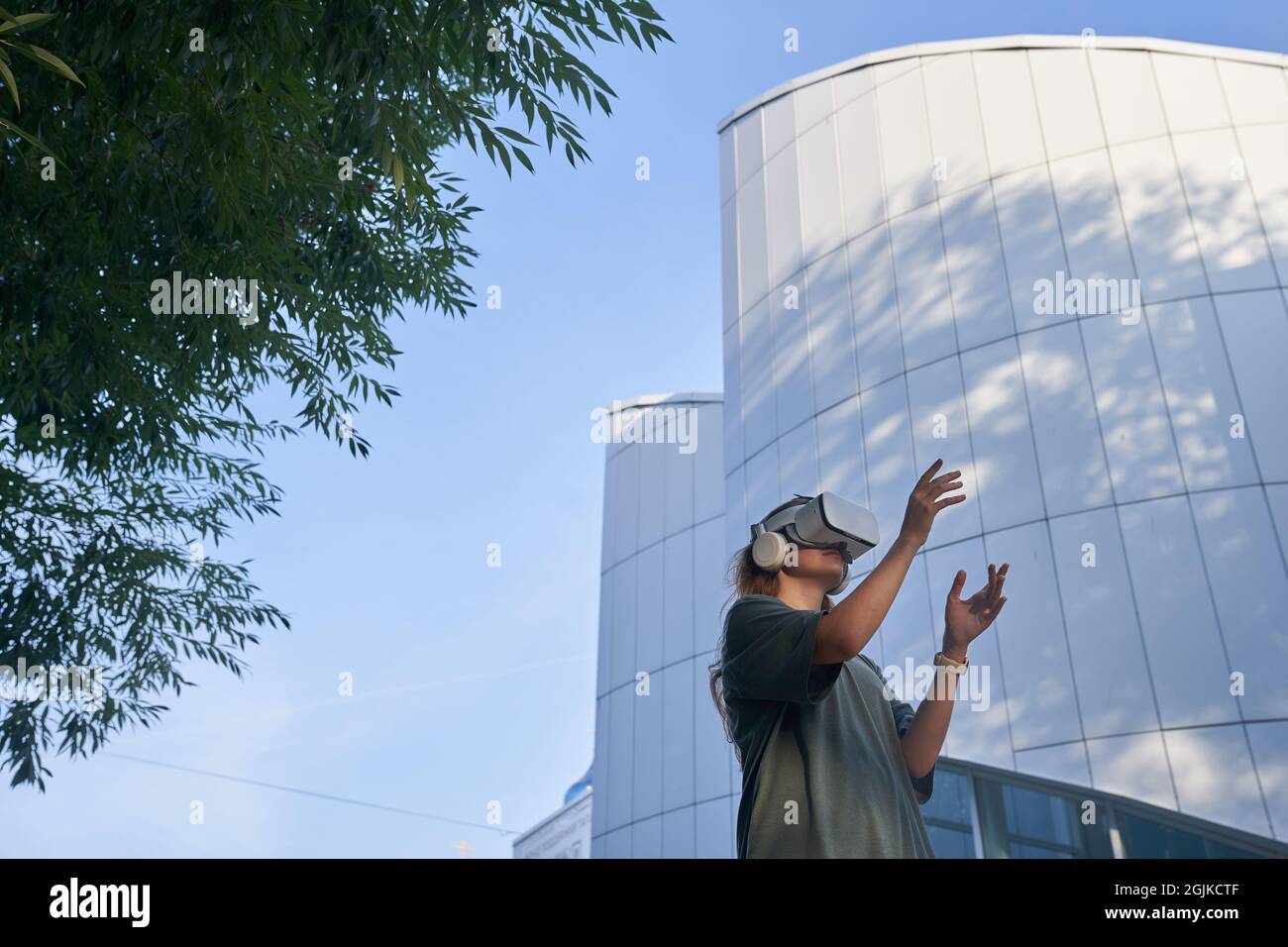 Una ragazza si sta divertendo in occhiali di realtà virtuale, in piedi sullo sfondo di un edificio a specchio. Il concetto del futuro. Foto di alta qualità Foto Stock