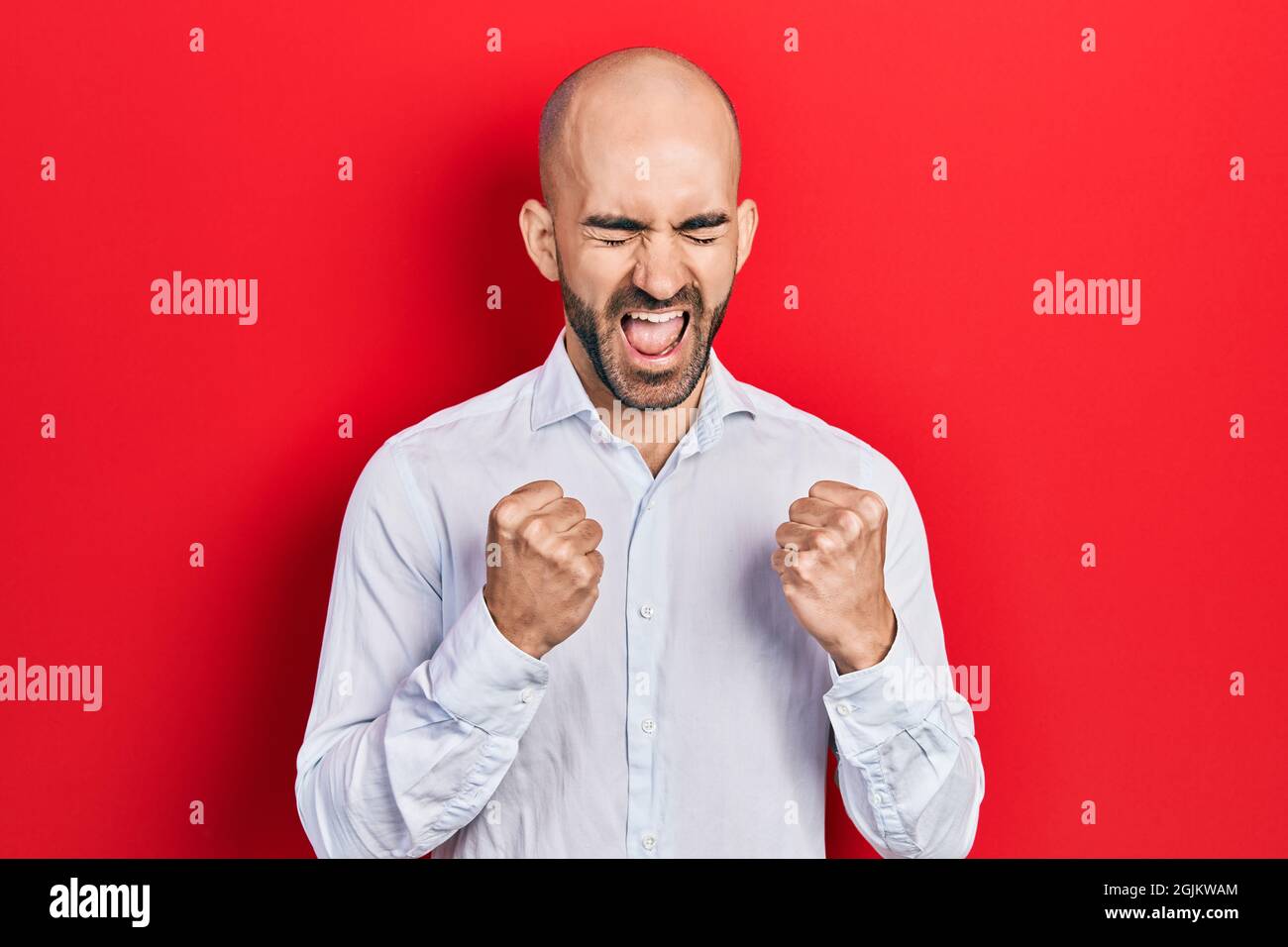 Giovane uomo calvo che indossa abiti eleganti che festeggia sorpreso e stupito per il successo con le braccia sollevate e gli occhi chiusi Foto Stock