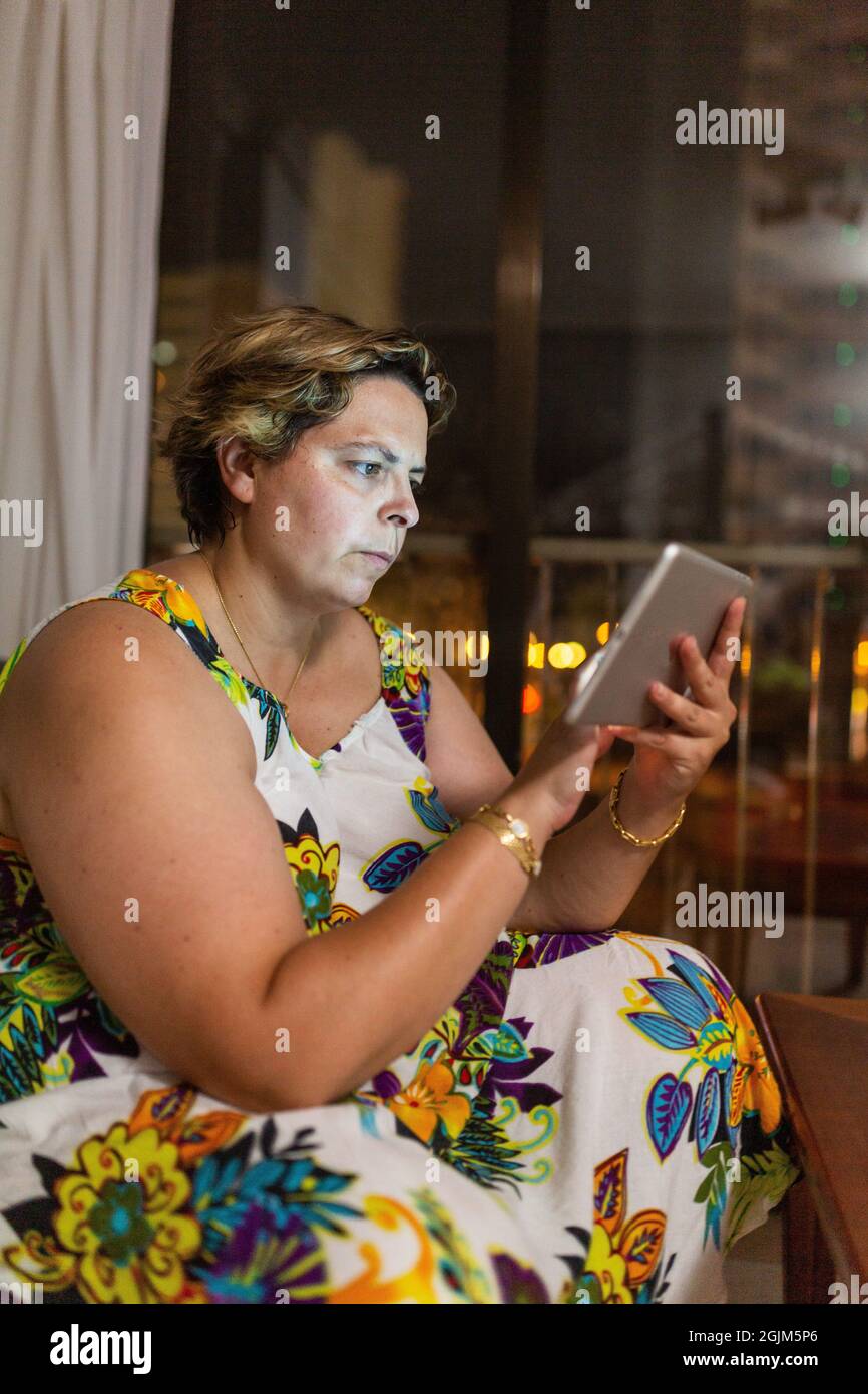 donna sovrappeso seduta sul divano con il tablet in mano, Foto Stock