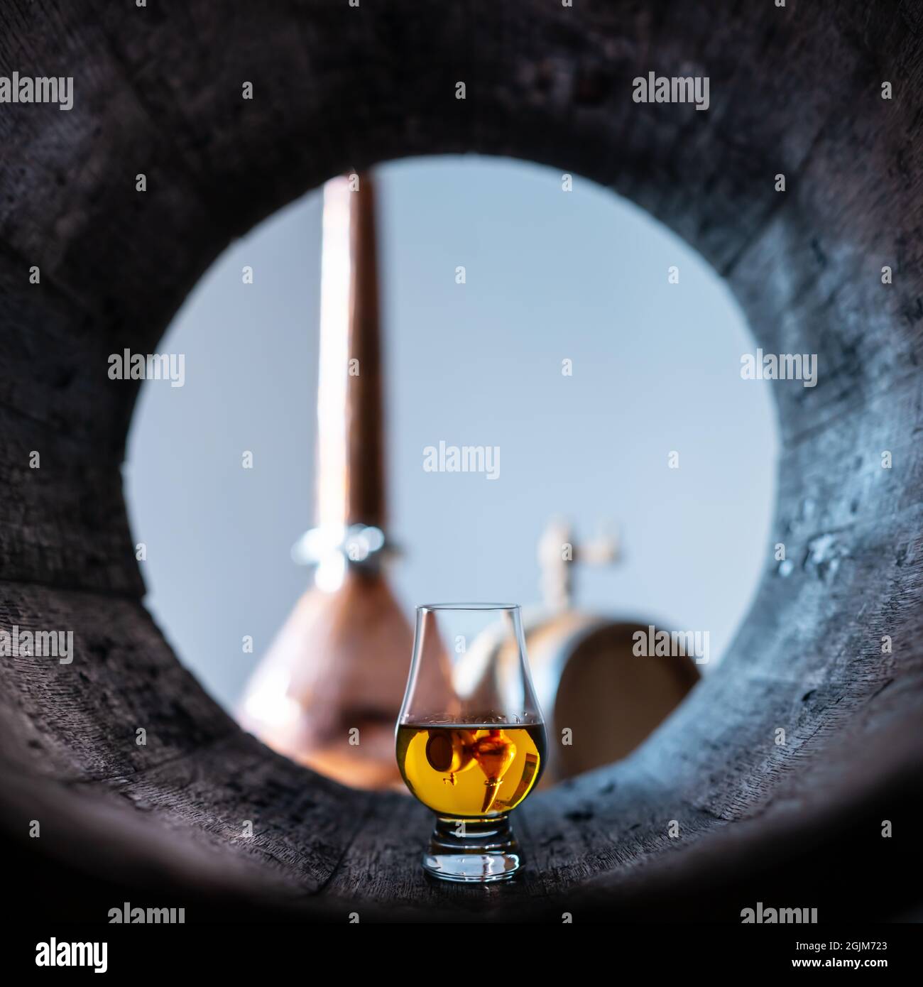 Un bicchiere di whisky in un vecchio barile di quercia. Rame alambic sullo sfondo. Tradizionale concetto di distilleria alcolica Foto Stock