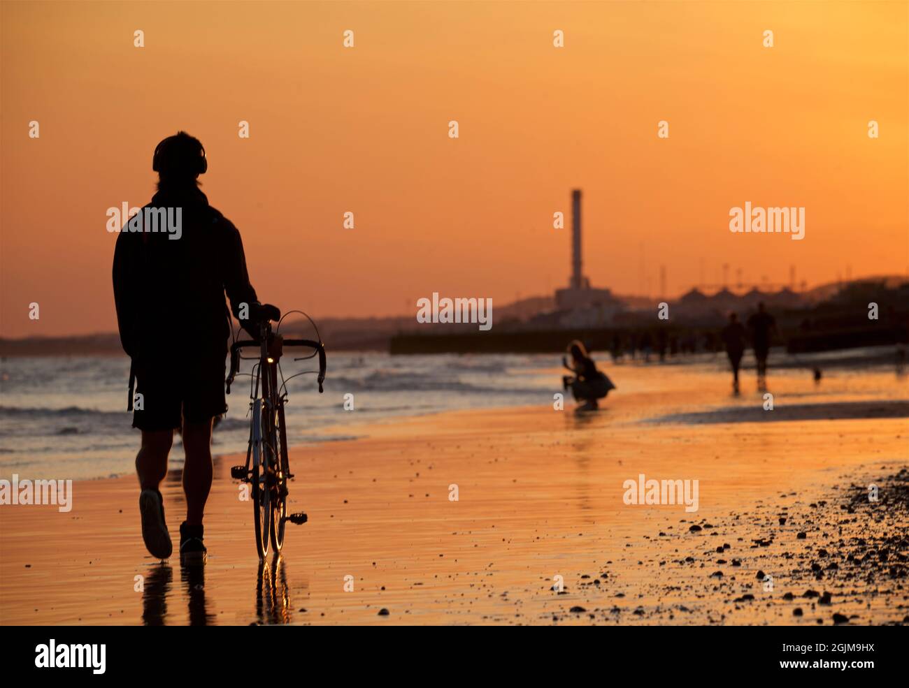 Spiaggia di Brighton e Hove in bassa marea. Silhouette di persone che camminano lungo la spiaggia sabbiosa al tramonto. Sussex orientale, Inghilterra. Centrale elettrica di Shoreham in lontananza Foto Stock