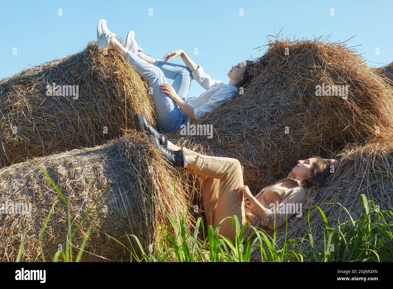 Due giovani donne bruna e bionda giacciono sui rotoli di fieno. Romantiche ragazze di campagna sul fieno. Foto Stock
