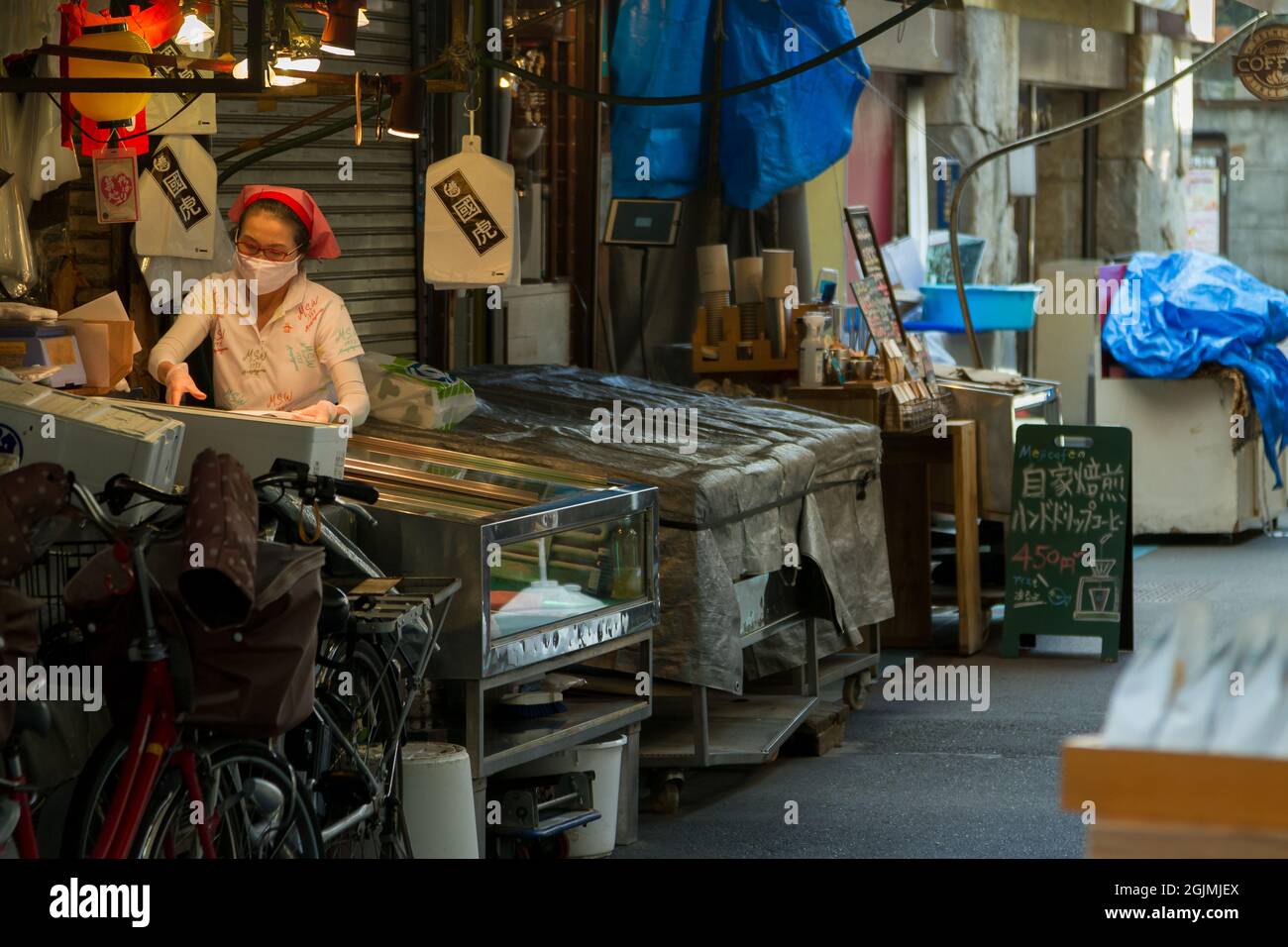 Una donna che lavora al banco di un piccolo negozio di pesce a Tsukiji mercato esterno Tokyo, Giappone Foto Stock