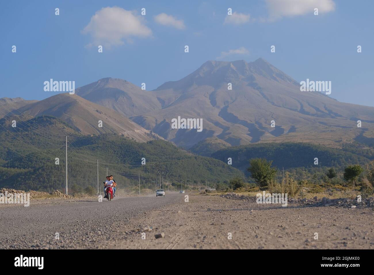 Aksaray. Turchia. Un Audi bianco e uomo in moto guida in strada sporca con nube di polvere dietro di esso e magnifica ed enorme montagna di Hasan Foto Stock Aksaray. Turchia. Un Audi bianco e uomo in moto guida in strada sporca con nube di polvere dietro di esso e magnifica ed enorme montagna di Hasan Foto Stock