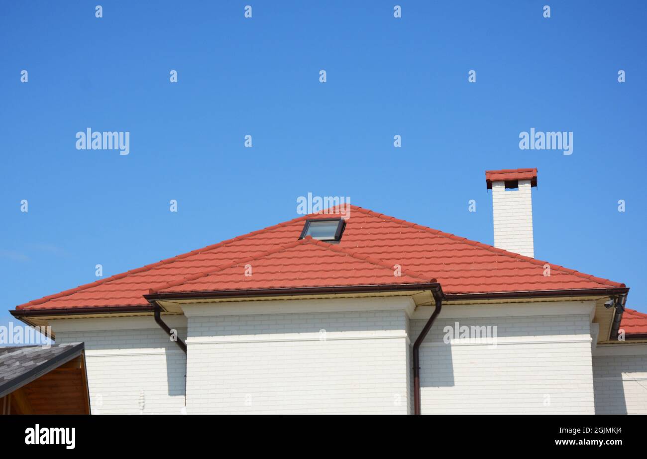 Primo piano su casa attico lucernario finestra con tetto in metallo rosso, grondaia, camino e telecamere di sicurezza. Foto Stock
