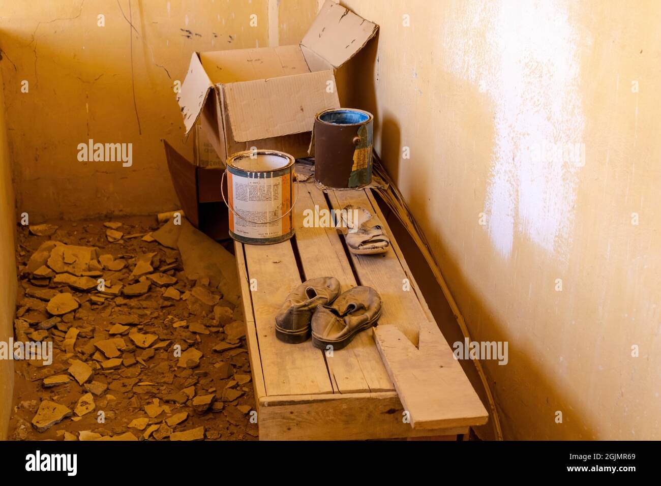 Lattine con vernice, scatola di cartone, e scarpe vecchie sul banco di legno nella casa abbandonata Foto Stock