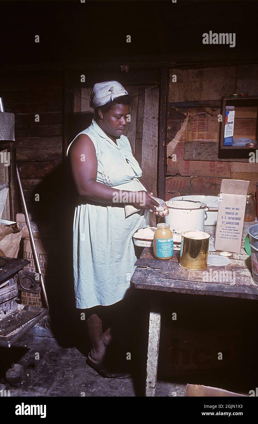 USA Georgia 1967. Una donna afroamericana nella sua casa in Georgia che prepara un pasto. Raffigurato in cucina con una stufa a sinistra. Un pacchetto di latte secco non grasso donato da noi departmen dell'agricoltura è visibile, che era una consegna ai poveri. Ambiente visibilmente povero. Kodachrome vetrino originale. Credit Roland Palm Ref 6-5-3 Foto Stock
