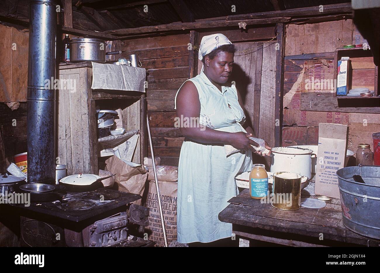 USA Georgia 1967. Una donna afroamericana nella sua casa in Georgia che prepara un pasto. Raffigurato in cucina con una stufa a sinistra. Un pacchetto di latte secco non grasso donato da noi departmen dell'agricoltura è visibile, che era una consegna ai poveri. Ambiente visibilmente povero. Kodachrome vetrino originale. Credit Roland Palm Ref 6-5-2 Foto Stock