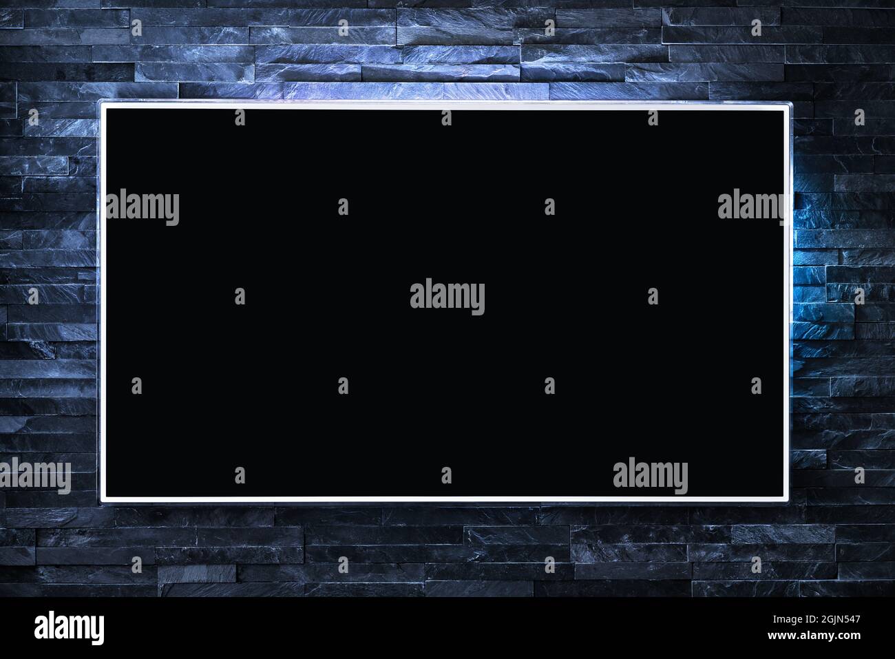 Schermo TV a parete di notte al buio con luce LED. Televisore e schermo piatto smart monitor su sfondo di mattoni blu. Loft moderno e futuristico. Foto Stock