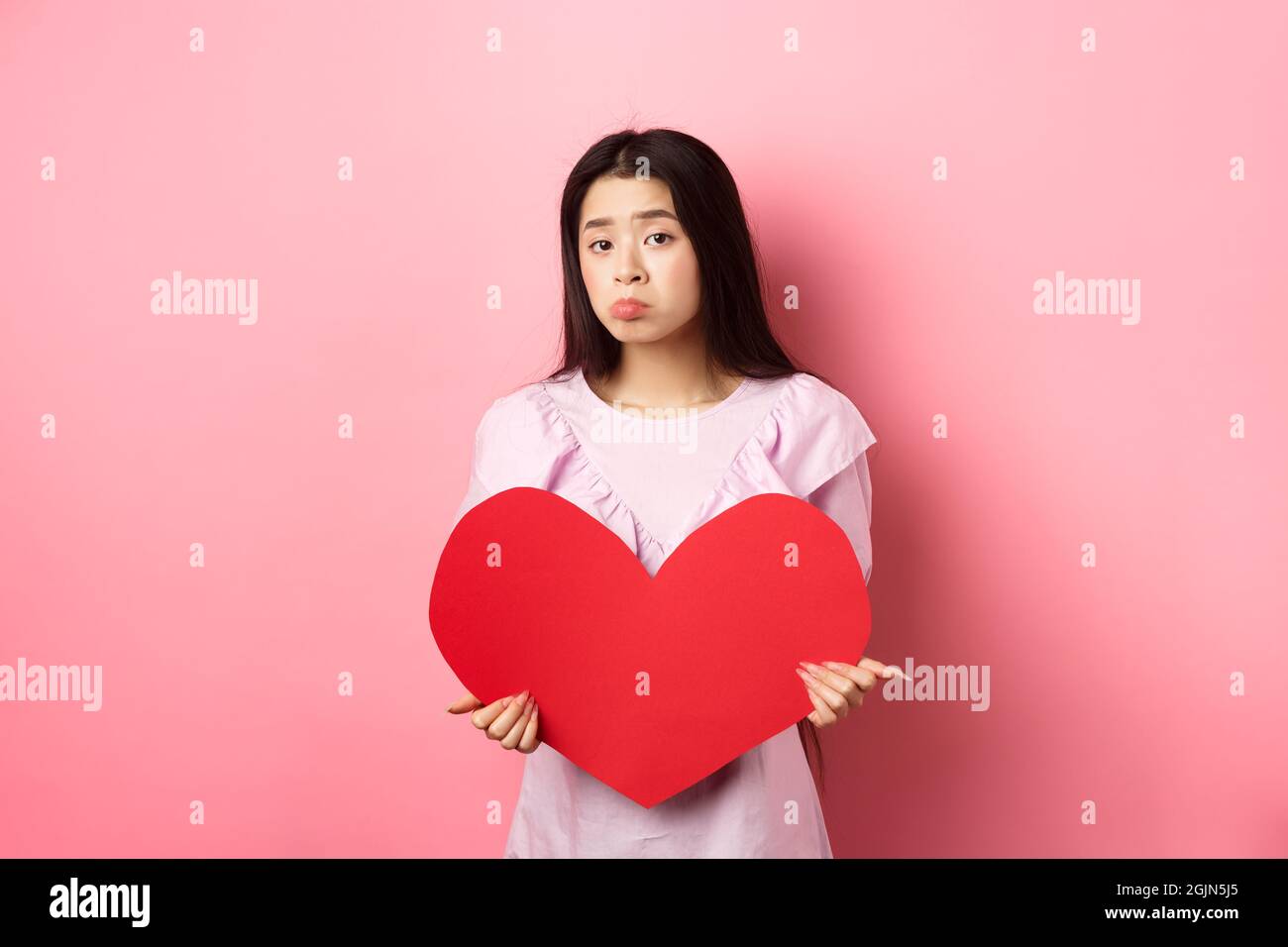 Concetto di San Valentino. Single teenage asian girl vuole innamorarsi, guardando triste e solitario alla macchina fotografica, sulking afflitto in festa degli amanti, tenendo grande Foto Stock