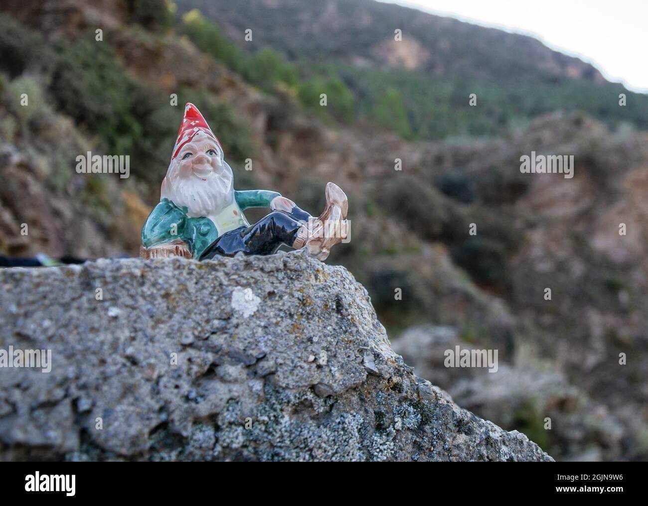 gnome adagiato su una pietra e montagne sullo sfondo con vegetazione Foto Stock