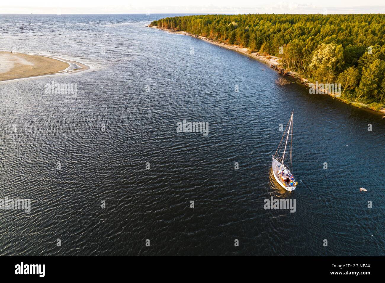 Vista dall'alto, splendida vista aerea di vela bianco lusso moderno non grande barca a vela o yacht con vela ripiegata a un estuario del fiume blu entra in mare vicino alla costa verde all'ora d'oro al tramonto Foto Stock