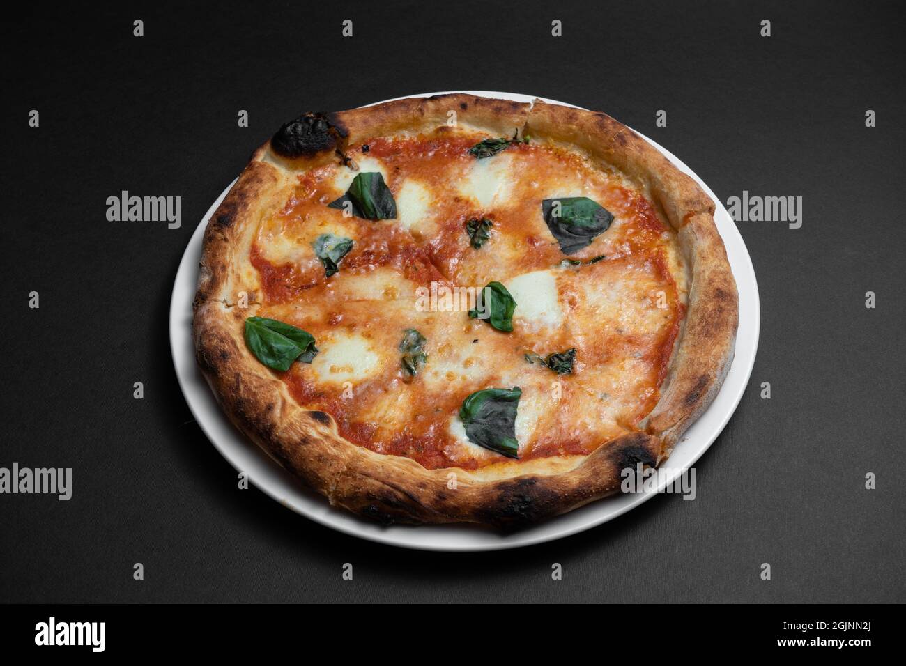 primo piano della pizza margarita con pomodori, formaggio e basilico su sfondo nero Foto Stock