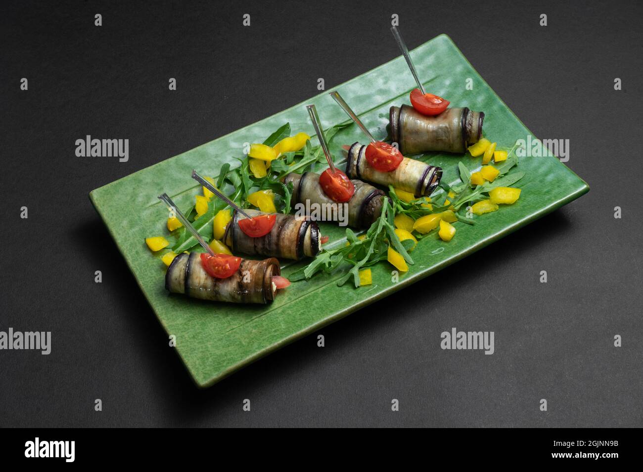 primo piano di involtini di melanzane con formaggio cremoso su piatto verde su sfondo nero Foto Stock