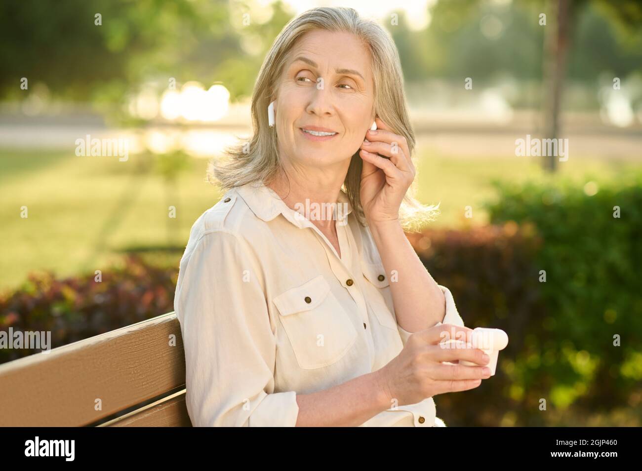 Donna adulta carina con cuffie sul banco Foto Stock