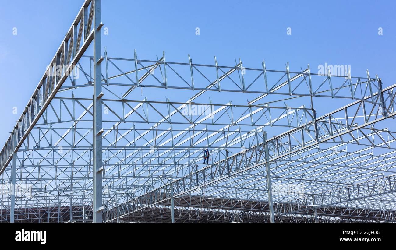 Nuove travi in acciaio per tetti di grandi dimensioni, montate insieme su un cantiere edile del magazzino di fabbrica con cielo blu. Foto Stock