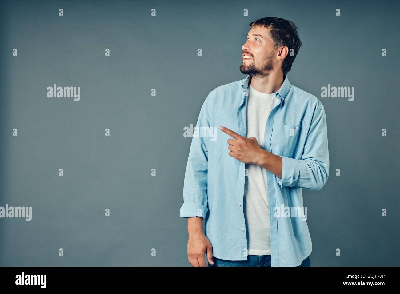 Un giovane caucasico sorride con una barba e punta il dito verso il lato dello spazio vuoto. Studio ritratto di un uomo su sfondo neutro. Pubblicità di beni o servizi. Foto Stock