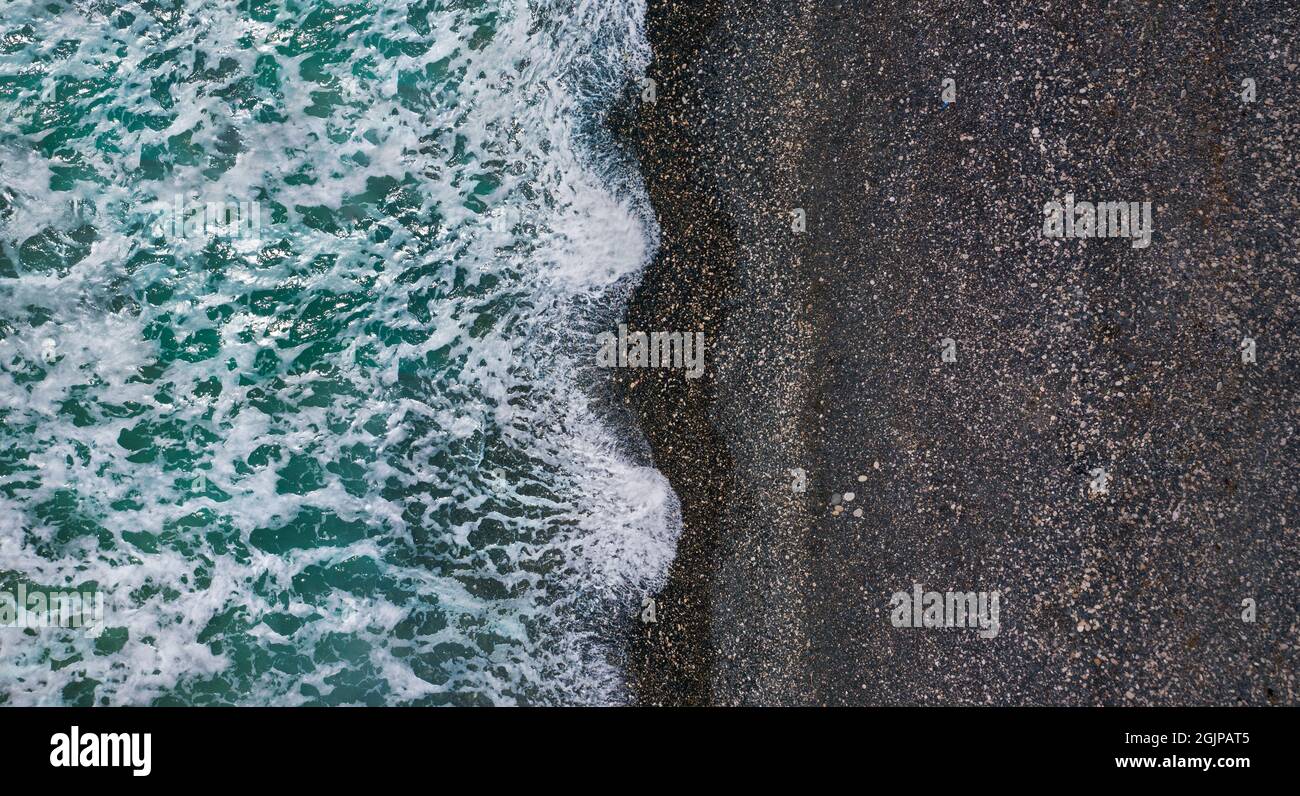 Onde drammatiche tempestose con schiuma di mare bianca su spiaggia di sabbia nera, struttura aerea del mare Foto Stock