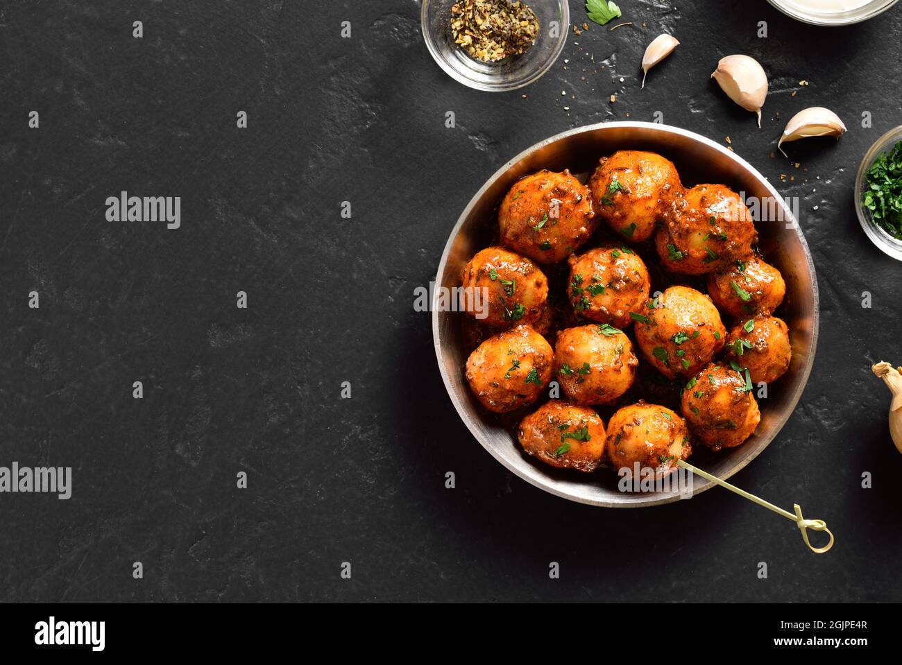 Padella le patate fritte del bambino con i semi di jeera e coriandolo in ciotola su sfondo scuro con spazio libero del testo. Popolare piatto indiano. Vista dall'alto, appartamento l Foto Stock
