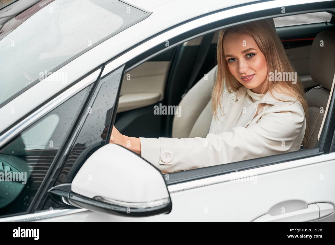 Bella giovane donna che guida auto moderna. Conducente seduto in auto e sorridente alla telecamera. Foto Stock