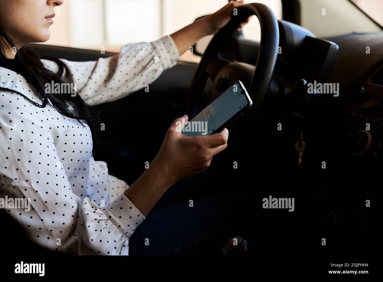 Giovane donna multirazziale testando e guidando auto. Donna che usa il cellulare mentre guida l'auto. Donna che usa lo smartphone mentre viaggia in auto. Guida Foto Stock
