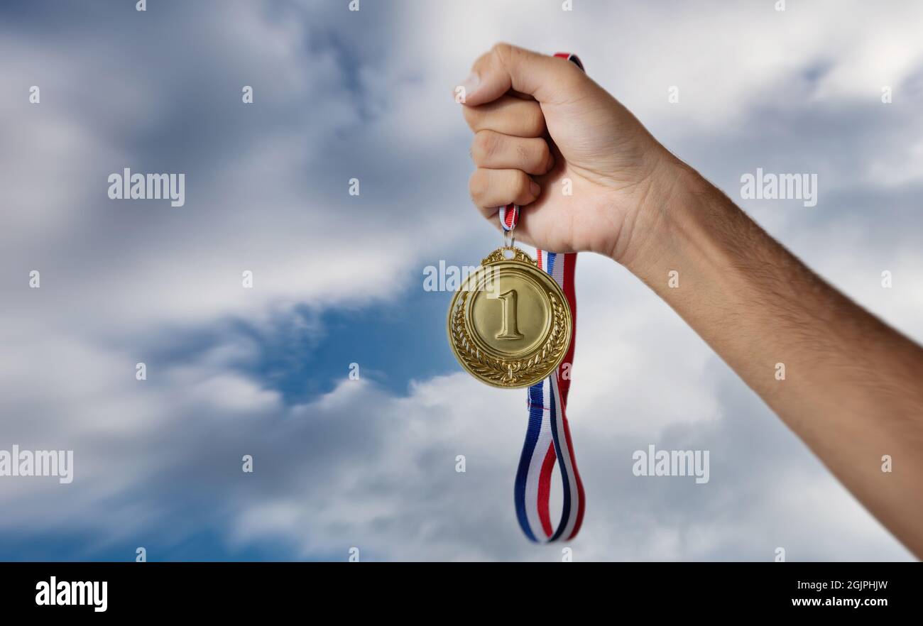 Mano che tiene la medaglia d'oro contro il cielo nuvoloso crepuscolo, in mano. Premio al primo posto sullo sfondo del cielo nuvoloso, atleta e vincitore del campione sportivo Foto Stock