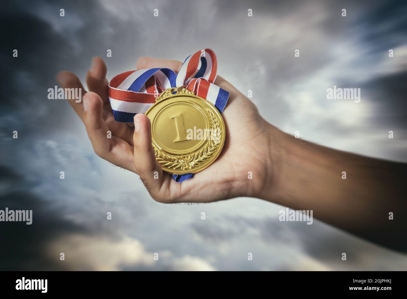 Medaglia per il primo posto nella palma dell'atleta contro un cielo drammatico. Vincitore del premio Gold. Concetto di vittoria e successo del campione sportivo Foto Stock