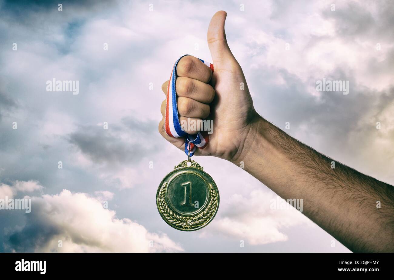 Medaglia e dump up per il primo posto contro un cielo drammatico. Vincitore del premio Gold. Concetto di vittoria e successo del campione sportivo Foto Stock