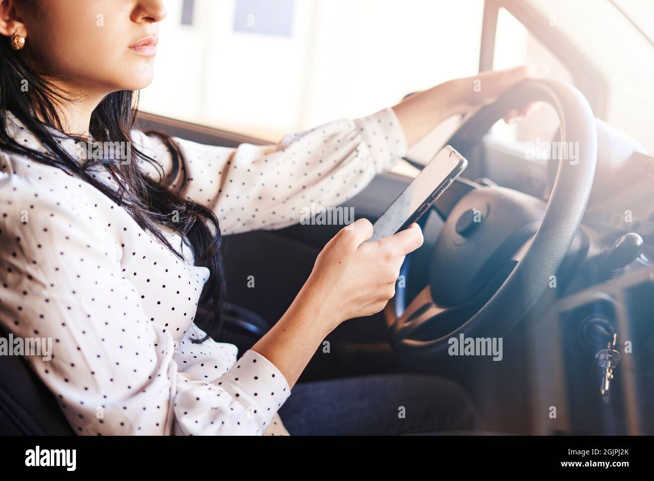 Giovane donna multirazziale testando e guidando auto. Donna che usa il cellulare mentre guida l'auto. Donna che usa lo smartphone mentre viaggia in auto. Guida Foto Stock