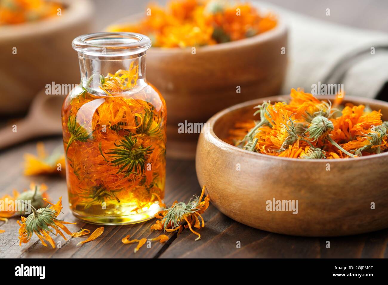 Bottiglia di olio essenziale di calendula, infusione o siero, ciotola di legno e mortaio di fiori sani essiccati di marigold. Medicina alternativa. Foto Stock