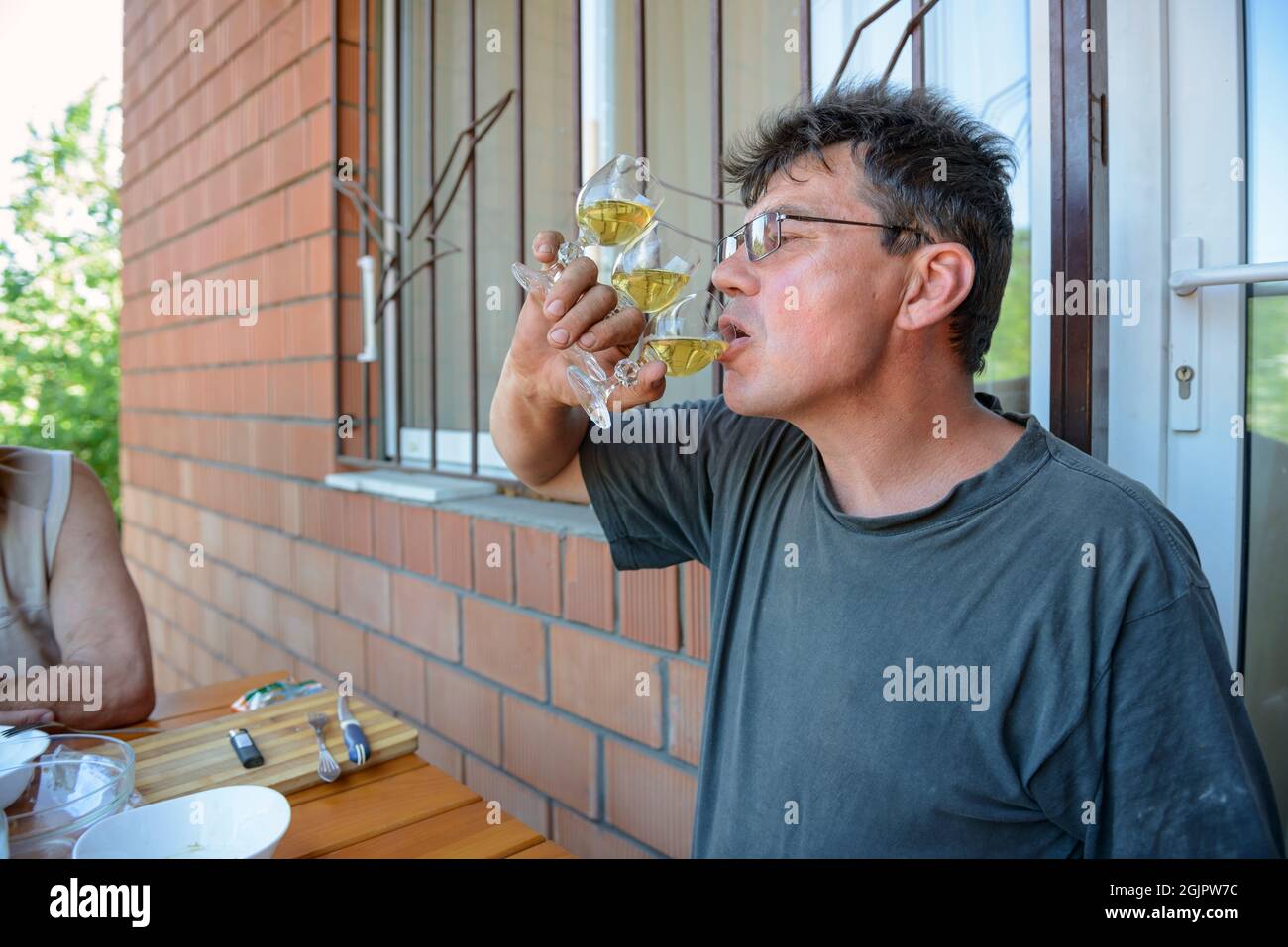 L'uomo maturo con i vetri sta bevendo tre vetri allo stesso tempo tenendoli in una mano. Foto Stock