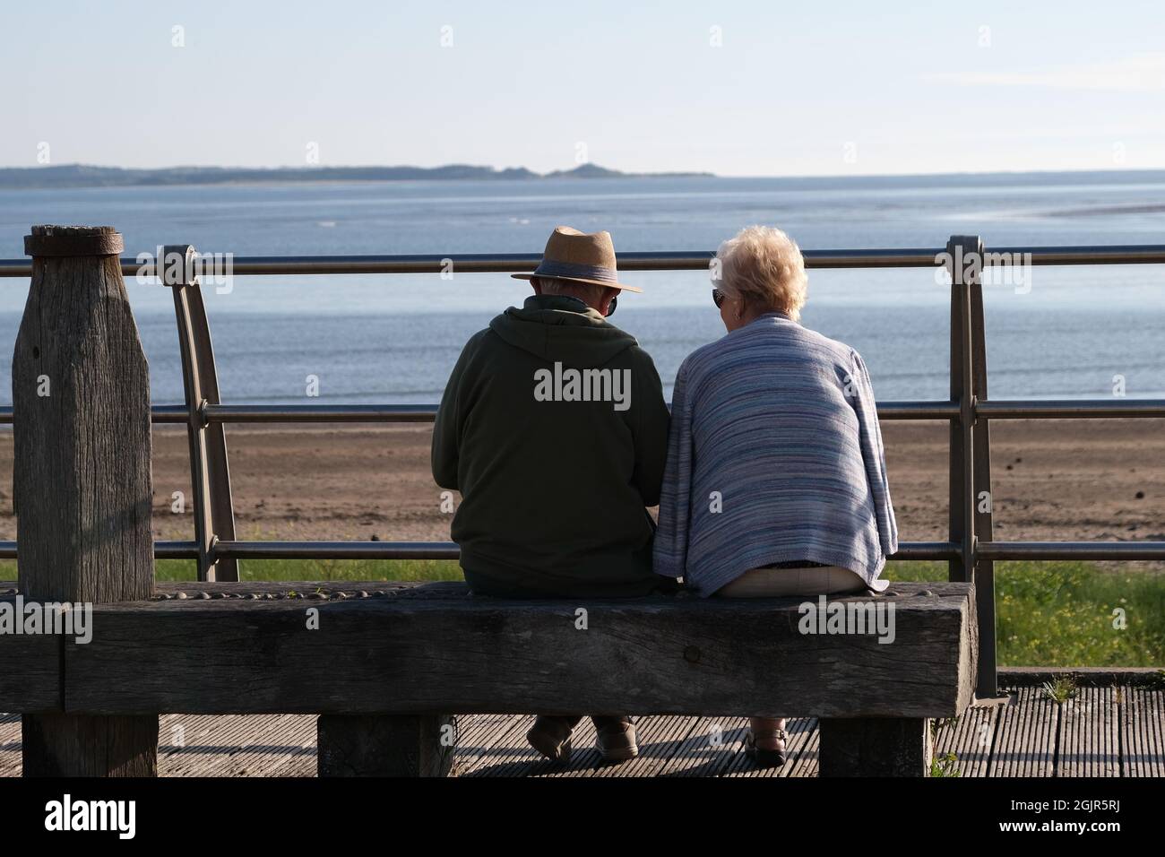 Un paio di età pensionabile seduti su una panchina su misura che si affaccia sulla spiaggia di llanelli e la penisola di Gower in lontananza Foto Stock